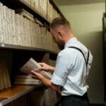 Pracownik archiwum w półformalnym stroju porządkuje teczki na regale