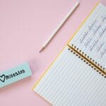 Zeszyt i gumka na pastelowym różowym tle z przekreślonymi słowami