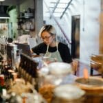 Barmanka przy barze pracuje na laptopie w otoczeniu butelek