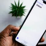 Dłoń trzymająca smartfon z otwartą skrzynką e-mail w tle newslettera