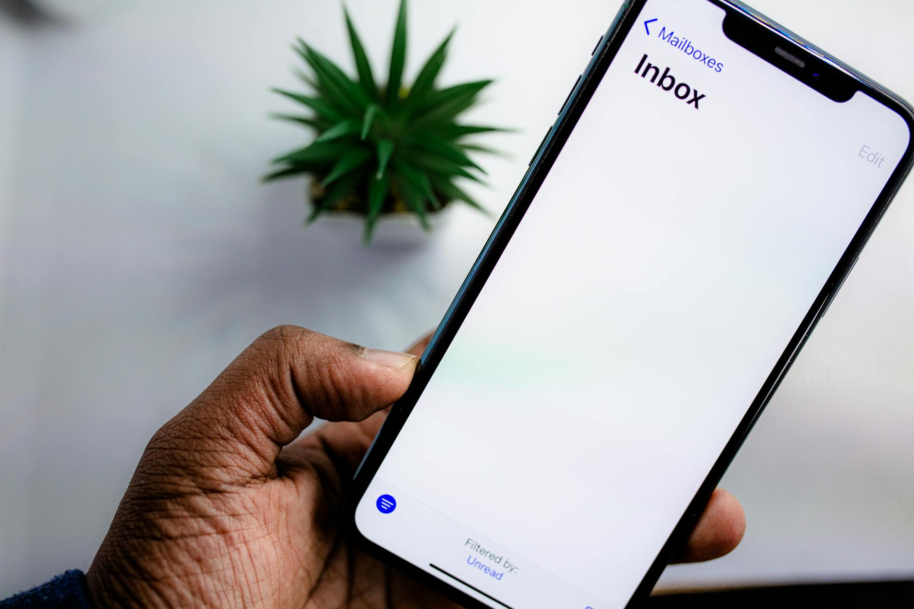 Dłoń trzymająca smartfon z otwartą skrzynką e-mail w tle newslettera