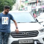 Mężczyzna w niebieskiej koszulce oparty o białe auto Hyundai w mieście