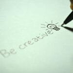Napis be creative z odręcznym rysunkiem żarówki na kartce