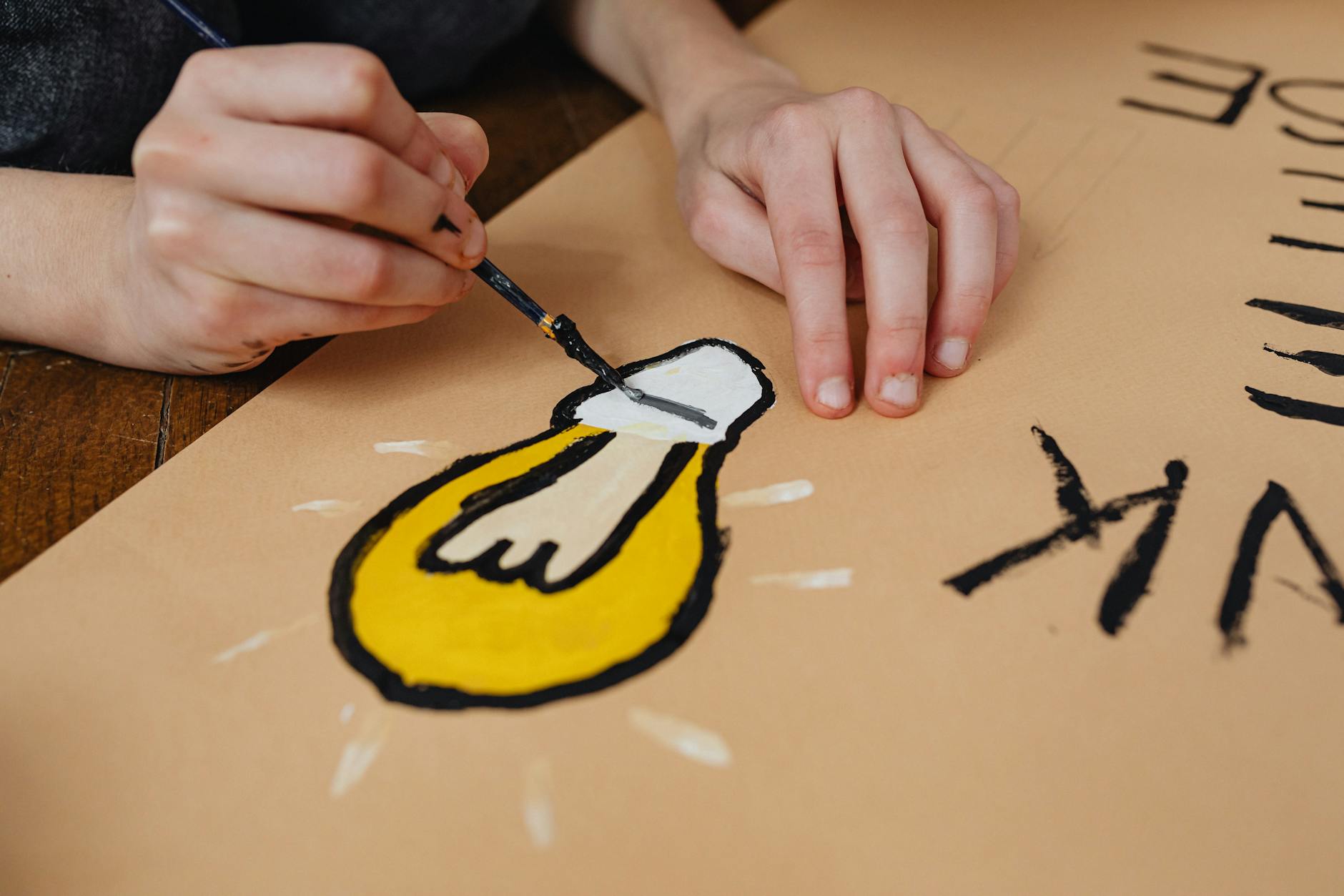 Ręka maluje farbami żarówkę na kartce jako projekt szkolny