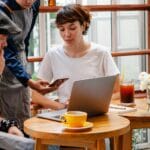 Zespół w kawiarni omawia projekty przy laptopie i smartfonie