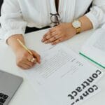 Bizneswoman podpisuje umowę przy biurku z laptopem i książką
