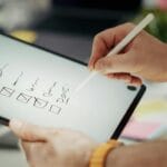 Dłoń z rysikiem zaznaczająca punkty na cyfrowej checkliście na tablecie