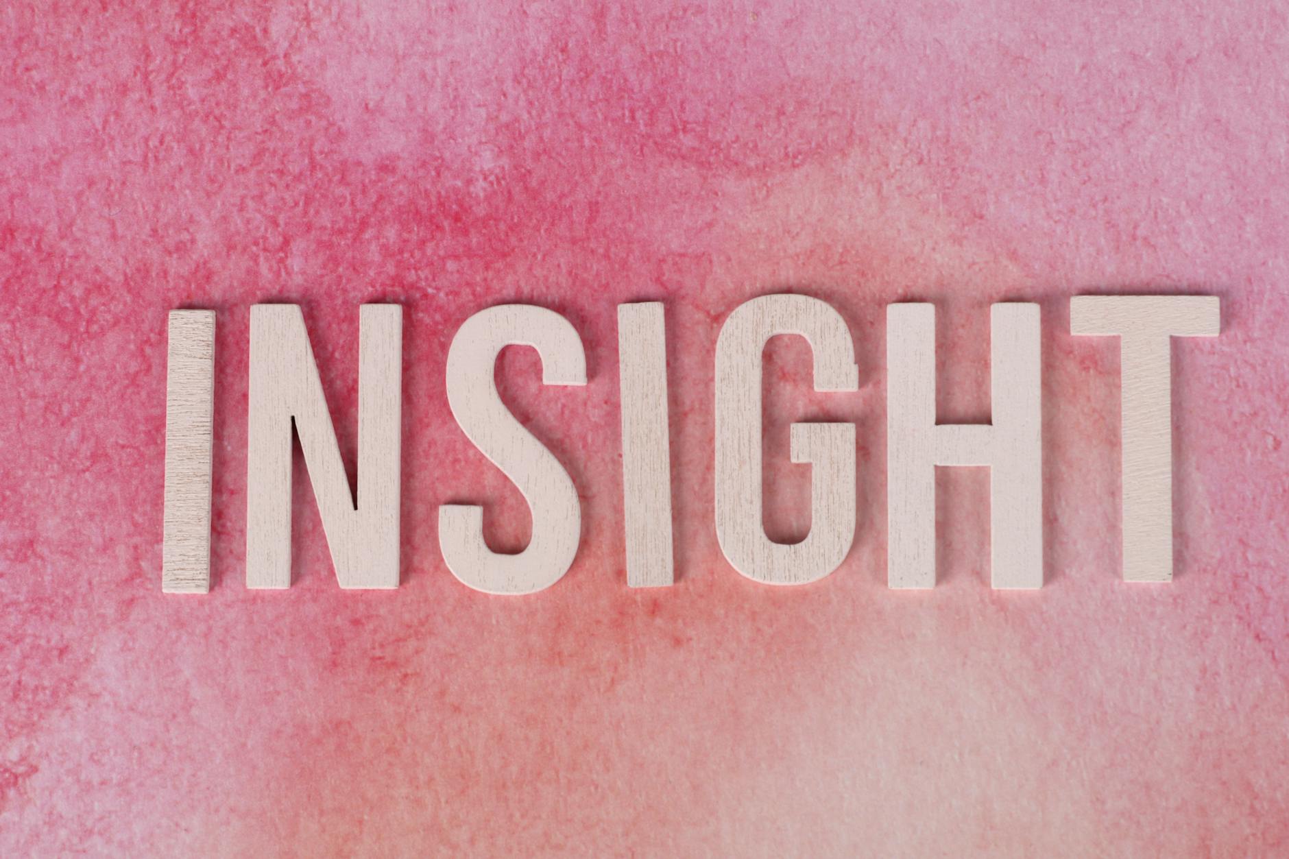 Drewniane litery tworzące napis INSIGHT na różowym tle akwarelowym