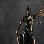 Figura Temidy z wagą i mieczem na ciemnym tle symbolizująca sprawiedliwość