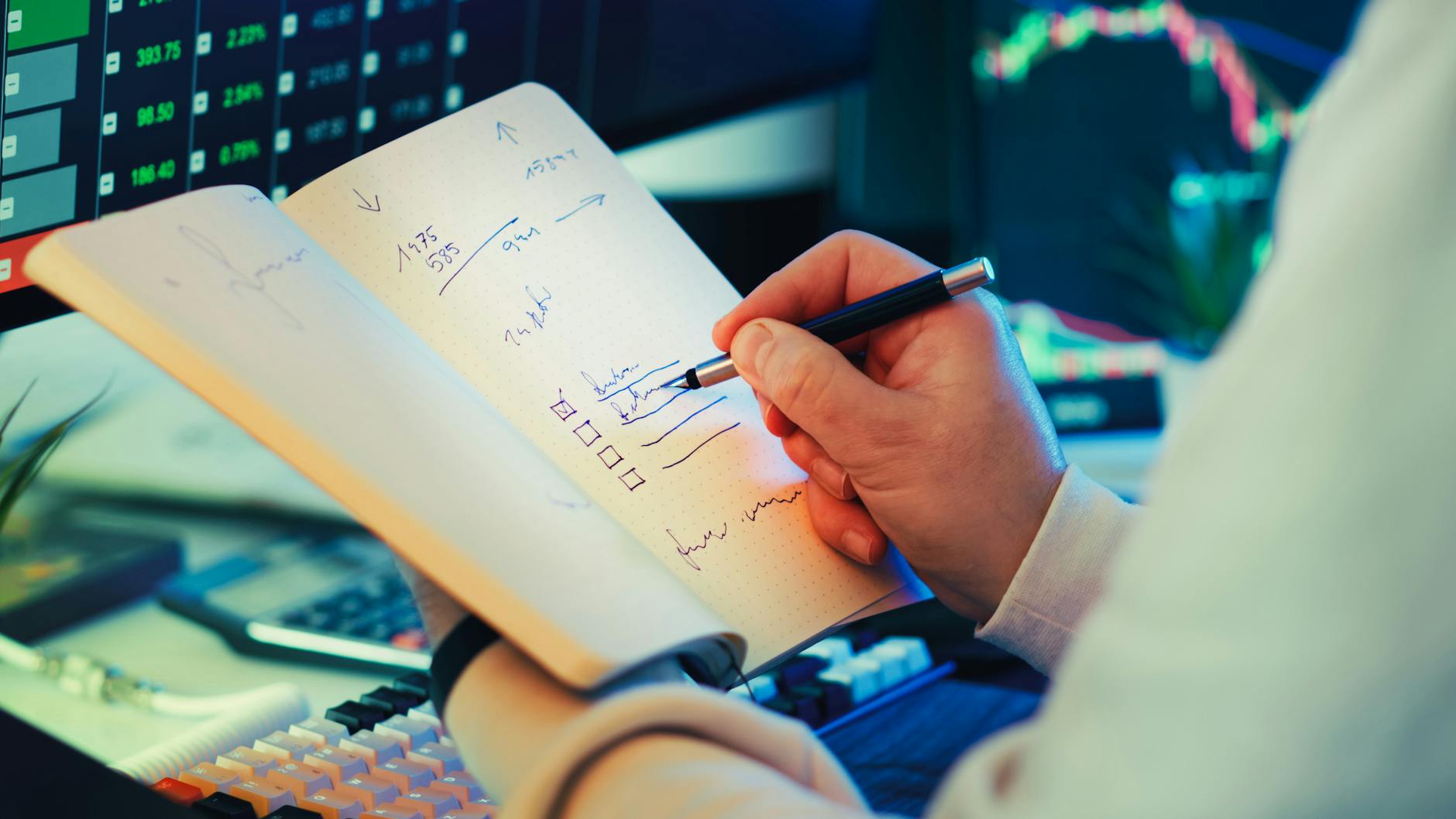 Mężczyzna robi notatki przy komputerze z wykresami giełdowymi