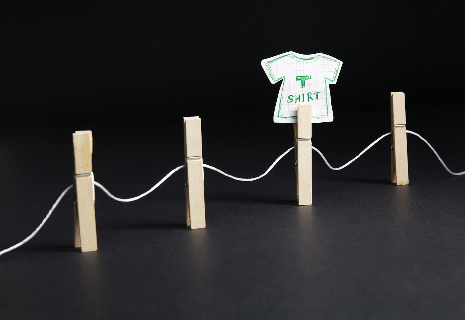 Papierowy t-shirt przypięty klamerkami na sznurku na ciemnym tle