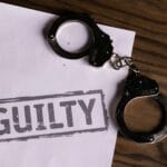 Kajdanki na kartce z napisem GUILTY symbolizujące winę za przestępstwo