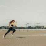 Kobieta w stroju sportowym biegnąca w słońcu po dachu budynku