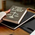 Książka The Law na drewnianym biurku obok złotych wag sprawiedliwości