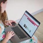 Kobieta w kwiecistej sukience robi zakupy online na laptopie z kartą
