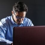 Mężczyzna w koszuli pracuje przy laptopie na szarym tle