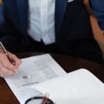 Jak ustalić dane anonimowego właściciela strony naruszającej prawa autorskie? Whois, hosting i Cloudflare Osoba podpisująca dokumenty prawne przy biurku w kancelarii